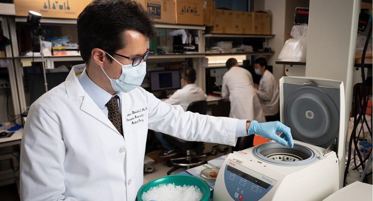 费迪南Skoulidis,医学博士博士。, conducting laboratory research while wearing his white coat and medical-grade face mask